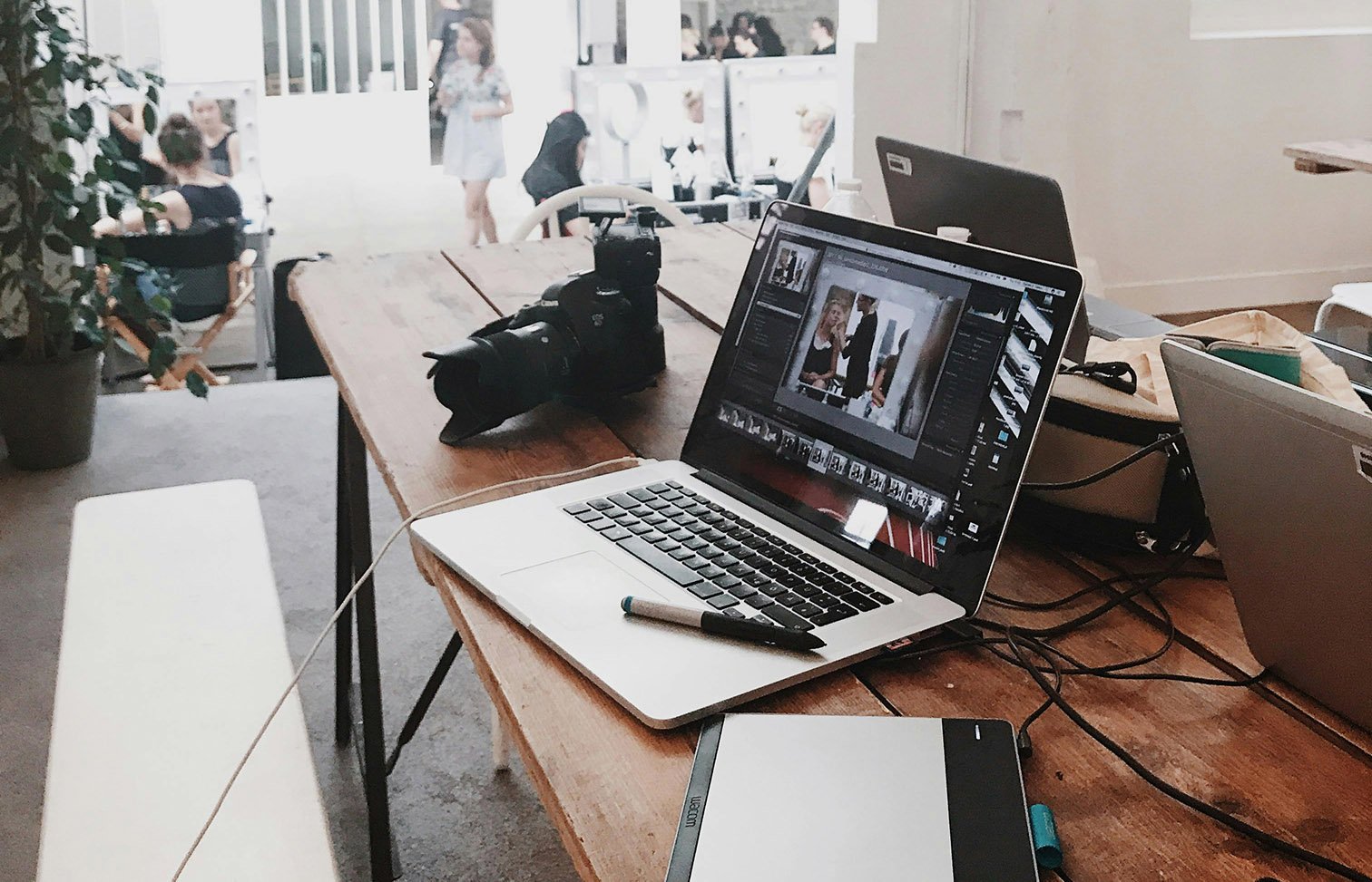 A photography studio with on a desk a camer, a laptop, and in the background active people.