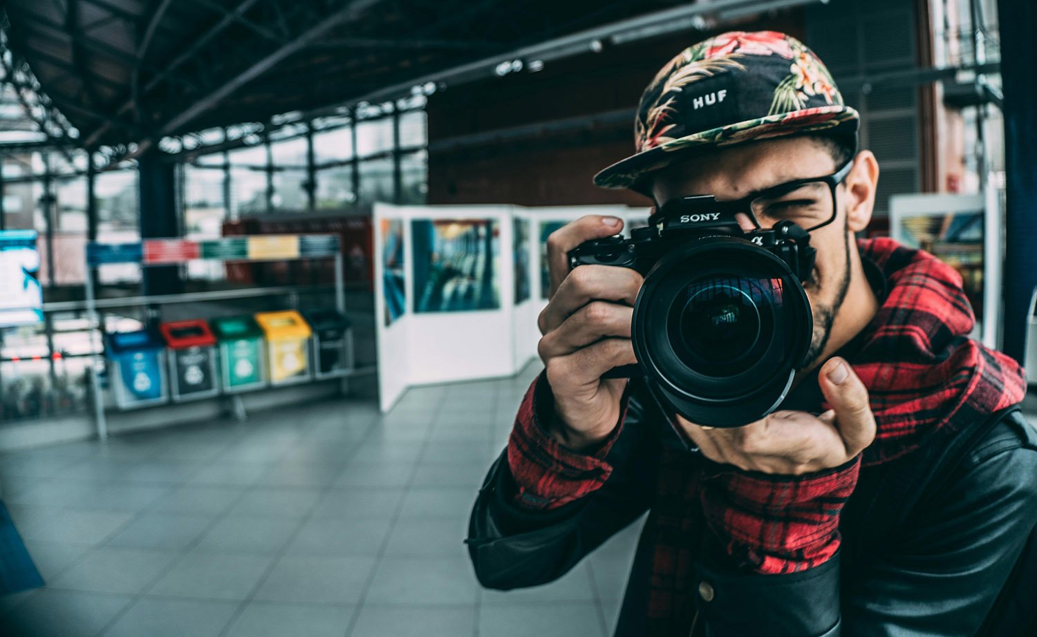 A photographer aiming his camera towards us, with in the background an art exhibition.