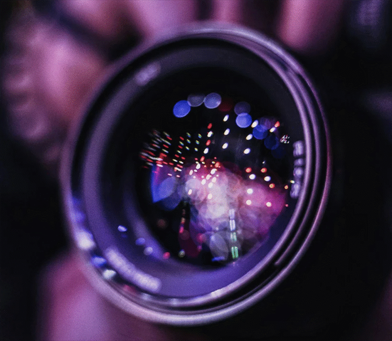 Close-up of a camera lens held to take a shot, with the street lights reflecting in it.